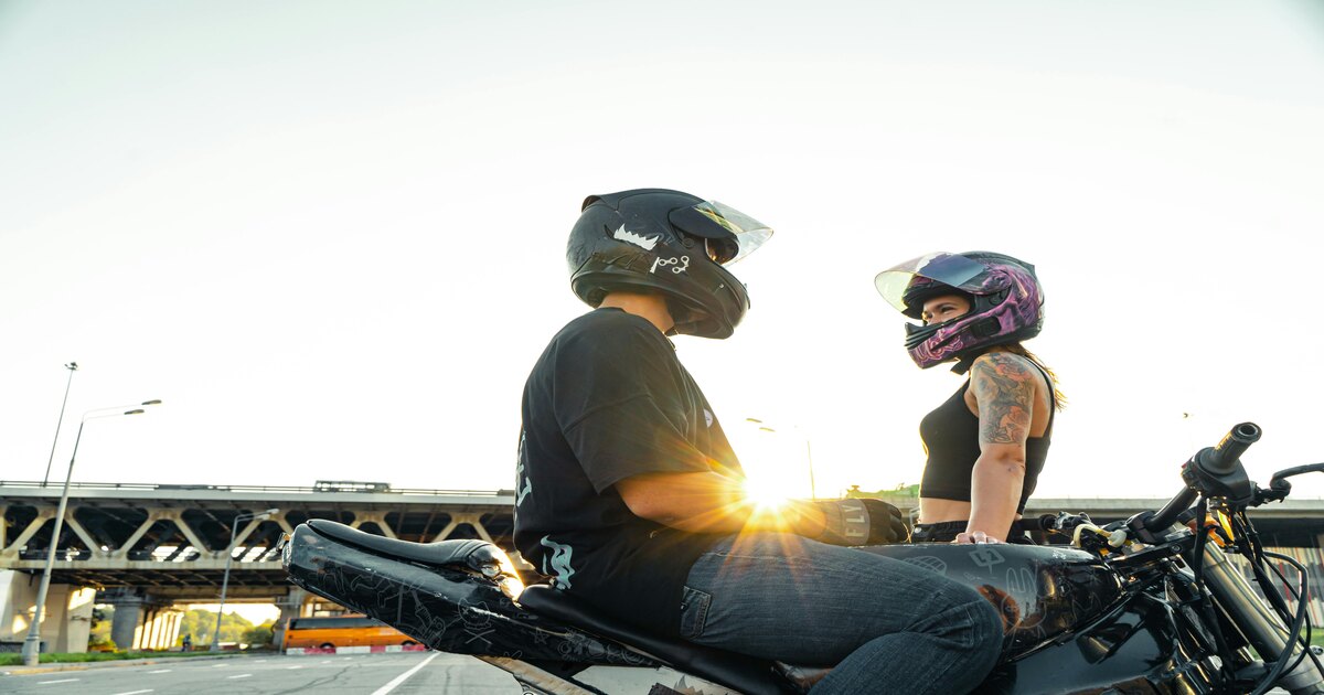 A man and a woman sitting on bikes wearing full-face motorcycle helmets with opened visors.