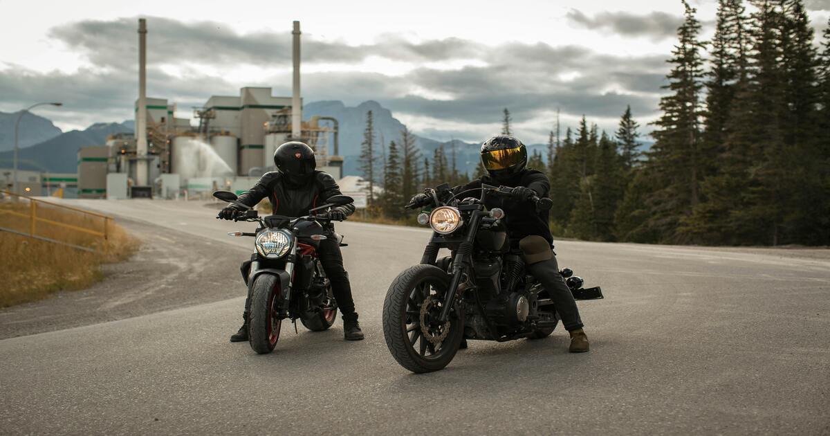 Two men riding motorcycles and discussing the differences between modular vs. full-face helmets.
