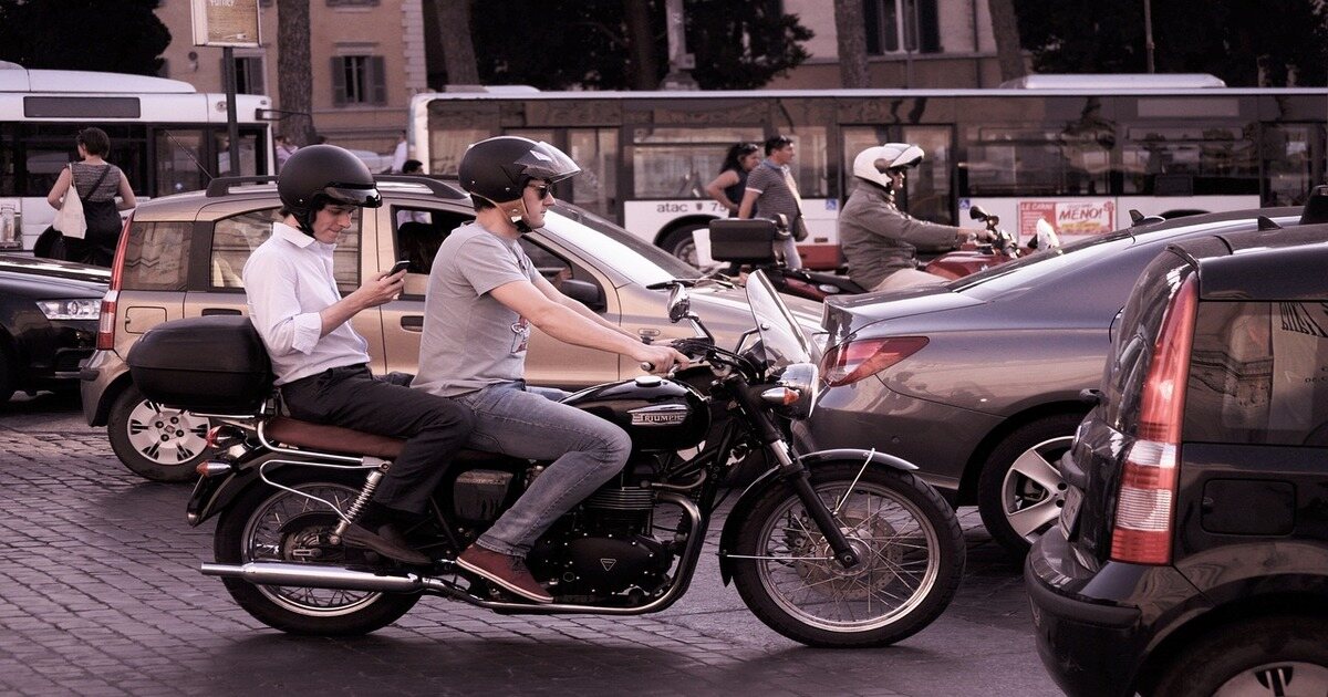 Two men riding on a motorcycle in traffic both wearing open-face helmets.