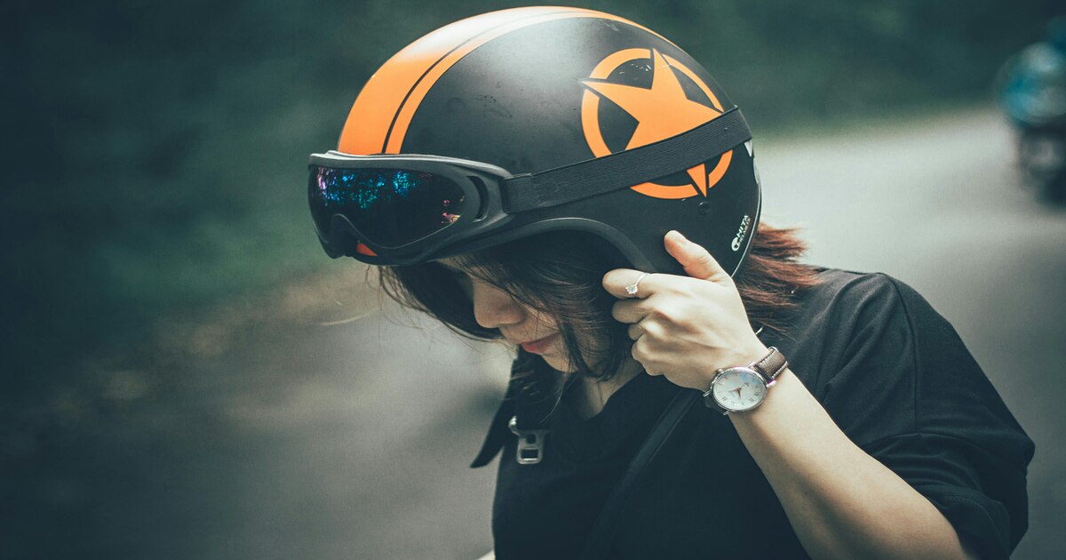 A close-up shot of a woman wearing a black and orange half-face helmet.
